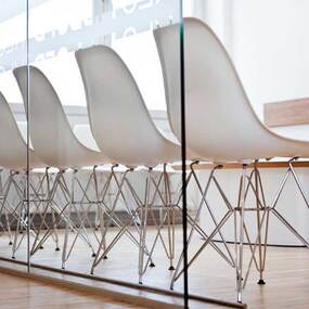 Moderne Wartezimmerstühle mit Holzfußboden und Glaswand in einer Zahnarztpraxis.