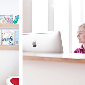 Helle, moderne Zahnarztpraxis mit freundlicher Empfangsdame und Wartebereich mit Kinderbüchern.